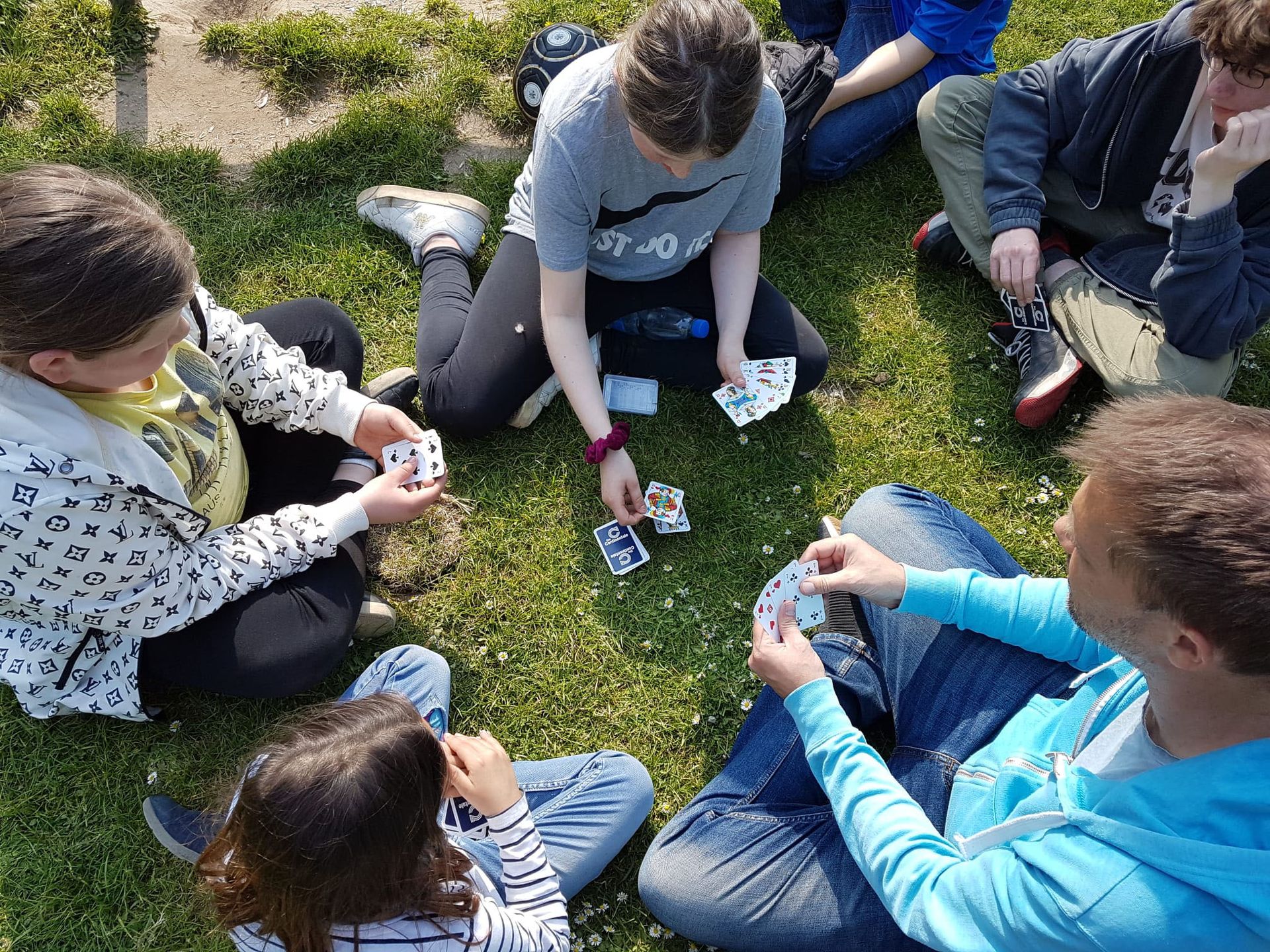 Jugendliche und Betreuende sitzen im Kreis auf einer Wiese und spielen gemeinsam Karten