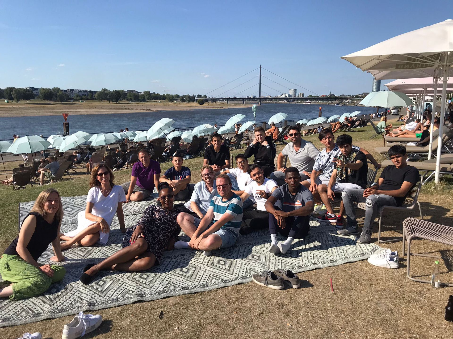 Eine große Gruppe Jugendlicher und Betreuender sitzt auf einer Picknickdecke am Rheinufer